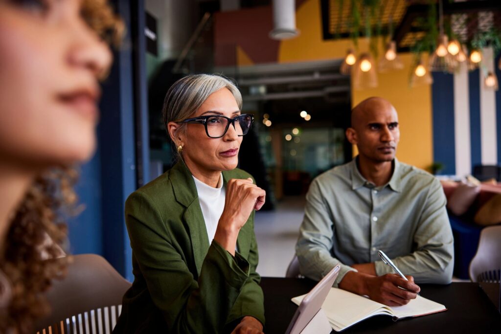 Confident female manager wearing glasses listening carefully in team meeting